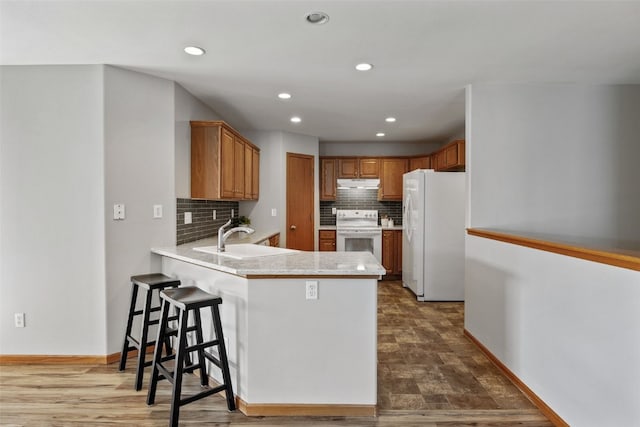 kitchen featuring white appliances, a peninsula, a sink, light countertops, and under cabinet range hood