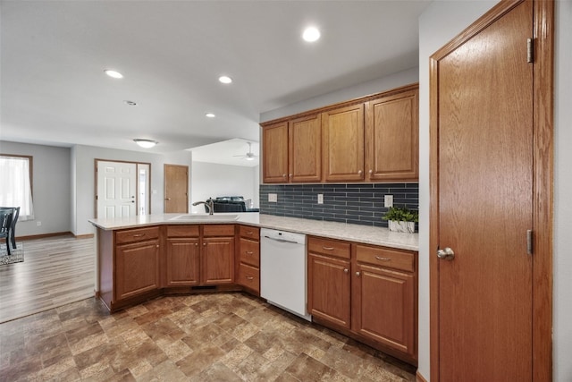 kitchen featuring a peninsula, white dishwasher, a sink, tasteful backsplash, and brown cabinets