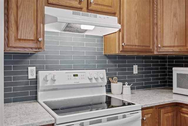 kitchen featuring under cabinet range hood, light countertops, decorative backsplash, brown cabinets, and white range with electric stovetop