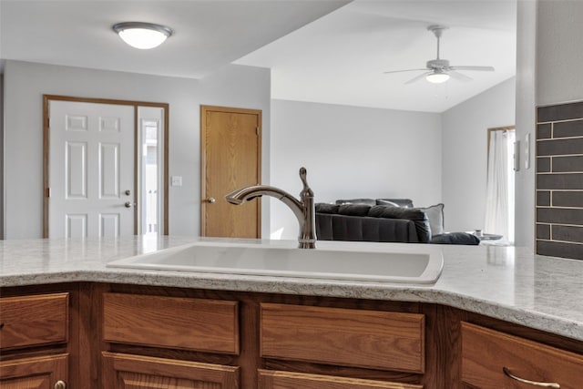 kitchen featuring ceiling fan, light stone countertops, lofted ceiling, brown cabinets, and a sink