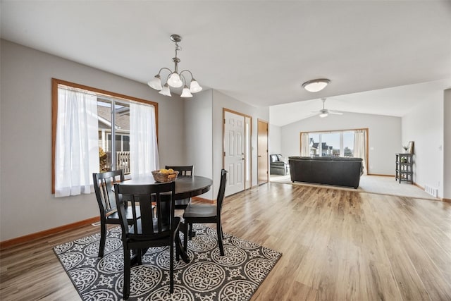 dining space featuring light wood-type flooring, lofted ceiling, baseboards, and ceiling fan with notable chandelier