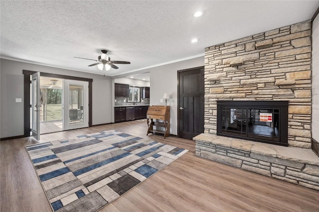 unfurnished living room featuring a ceiling fan, a textured ceiling, wood finished floors, a fireplace, and baseboards