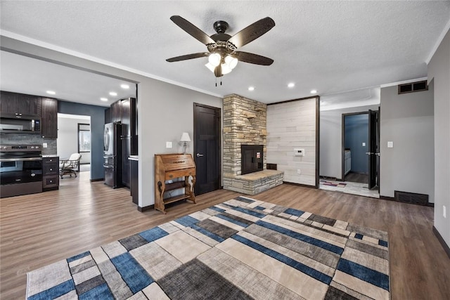 unfurnished living room featuring visible vents, a textured ceiling, a stone fireplace, light wood finished floors, and ceiling fan