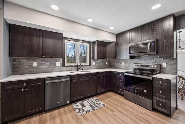 kitchen featuring dark brown cabinetry, appliances with stainless steel finishes, light wood-style floors, and a sink