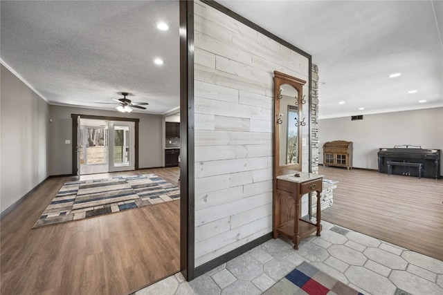 entrance foyer featuring ceiling fan, wood walls, ornamental molding, wood finished floors, and a textured ceiling