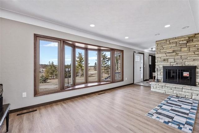 unfurnished living room with a fireplace, wood finished floors, visible vents, and baseboards