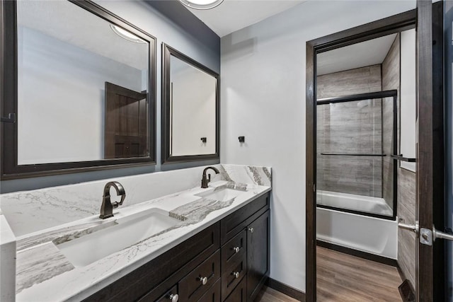 full bath with double vanity, wood finished floors, enclosed tub / shower combo, and a sink