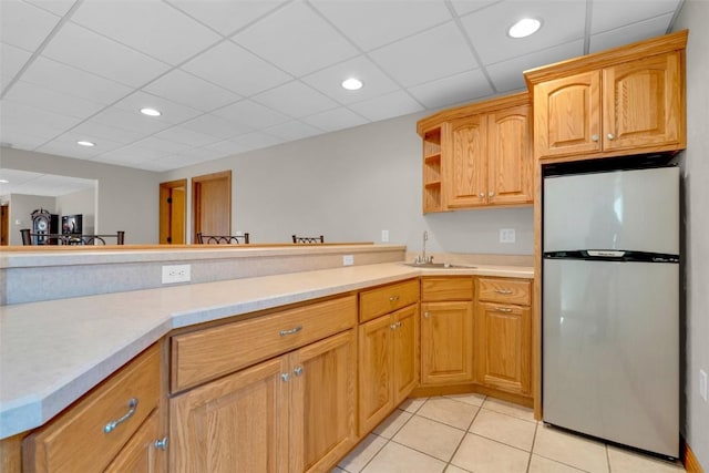 kitchen featuring a sink, light countertops, freestanding refrigerator, light tile patterned flooring, and open shelves