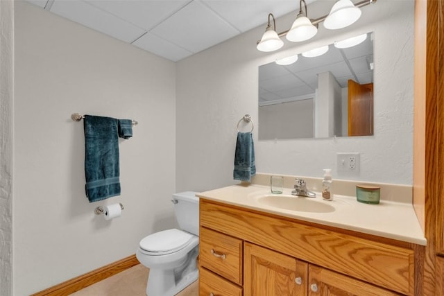 bathroom with toilet, a drop ceiling, tile patterned flooring, baseboards, and vanity