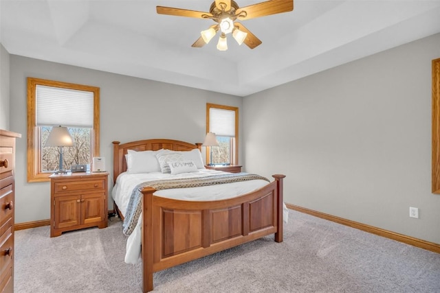 bedroom featuring baseboards, a raised ceiling, light colored carpet, and a ceiling fan