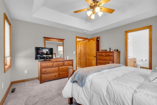 bedroom featuring baseboards, visible vents, a tray ceiling, ensuite bathroom, and light carpet