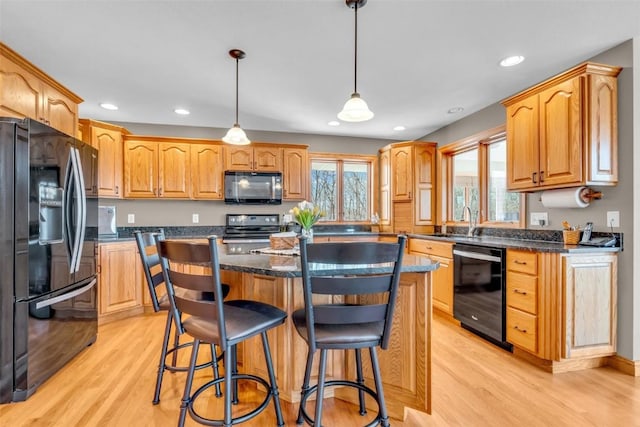 kitchen featuring light wood finished floors, a breakfast bar area, a center island, and black appliances