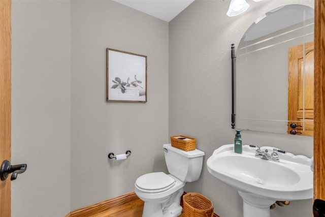 half bathroom featuring toilet, wood finished floors, baseboards, and a sink