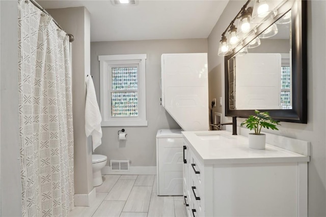 bathroom with visible vents, toilet, stacked washer and dryer, baseboards, and vanity