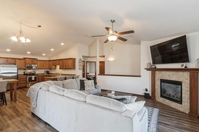 living room featuring a tiled fireplace, ceiling fan with notable chandelier, recessed lighting, dark wood-style flooring, and vaulted ceiling