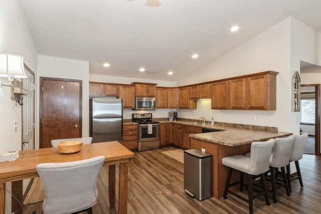 kitchen with vaulted ceiling, a peninsula, brown cabinetry, stainless steel appliances, and a sink