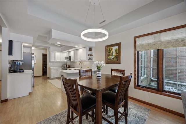 dining area with a tray ceiling, visible vents, baseboards, and light wood finished floors