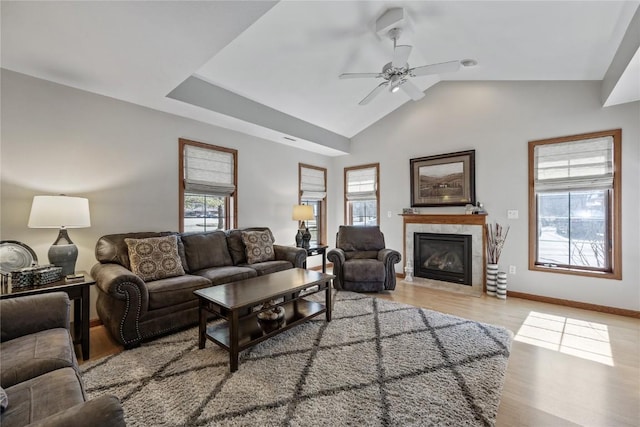 living area featuring a fireplace with flush hearth, light wood finished floors, baseboards, ceiling fan, and vaulted ceiling