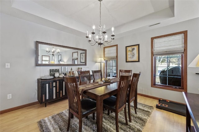 dining space featuring an inviting chandelier, light wood-style floors, visible vents, and a raised ceiling