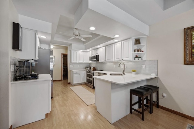 kitchen featuring a ceiling fan, a peninsula, a sink, stainless steel appliances, and light wood-type flooring