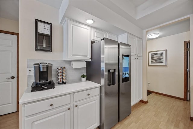 kitchen featuring baseboards, decorative backsplash, white cabinets, stainless steel refrigerator with ice dispenser, and light wood-type flooring