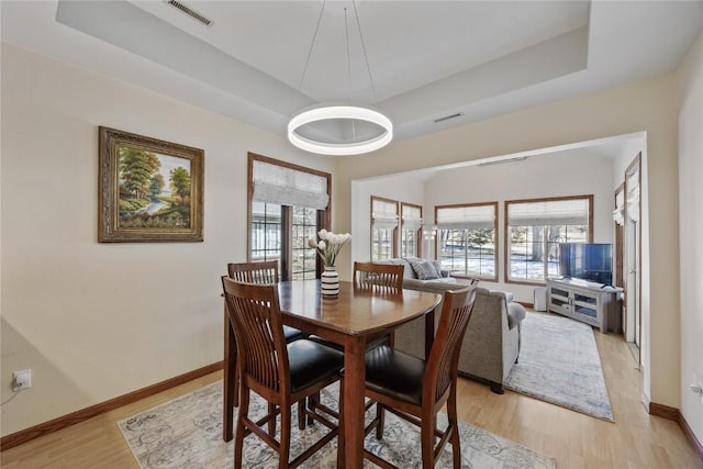 dining room featuring a wealth of natural light, a tray ceiling, visible vents, and light wood finished floors