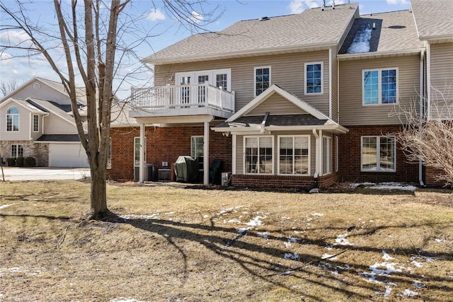 back of property with a balcony, roof with shingles, and brick siding