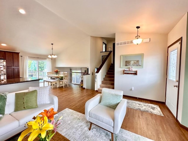 living room featuring visible vents, wood finished floors, a chandelier, stairs, and vaulted ceiling