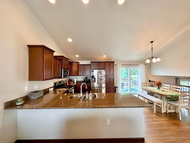 kitchen with light wood-type flooring, a sink, dark stone countertops, stainless steel appliances, and a peninsula