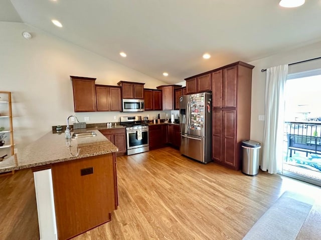 kitchen featuring a sink, light stone counters, light wood-style floors, appliances with stainless steel finishes, and a peninsula