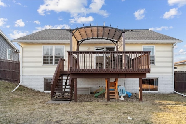 rear view of property featuring a playground, fence, stairs, roof with shingles, and a lawn