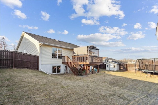 rear view of property featuring a trampoline, stairway, a fenced backyard, a deck, and an outbuilding