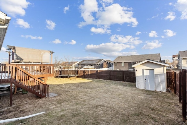 view of yard featuring an outbuilding, a shed, a wooden deck, a fenced backyard, and a trampoline