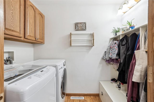 washroom featuring baseboards, visible vents, washing machine and clothes dryer, light wood-style flooring, and cabinet space