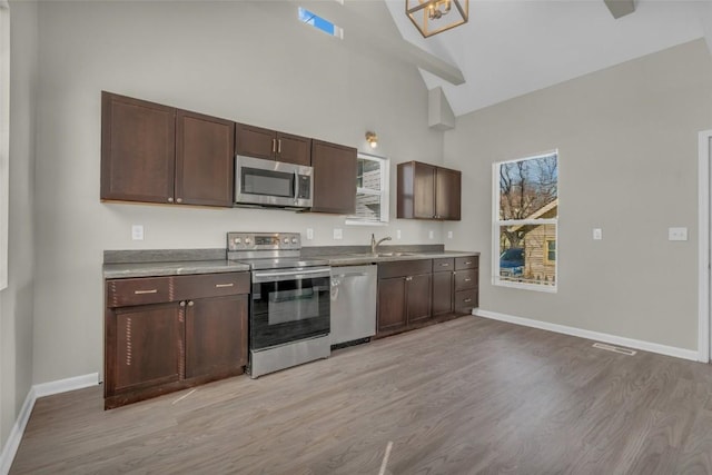 kitchen featuring stainless steel appliances, light wood-style floors, baseboards, and a sink