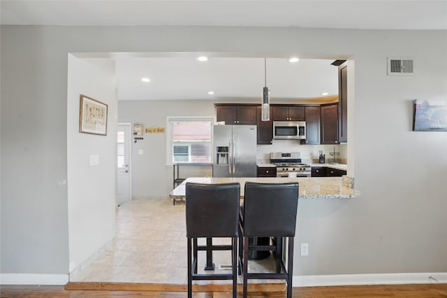 kitchen featuring visible vents, dark brown cabinets, a kitchen breakfast bar, a peninsula, and stainless steel appliances