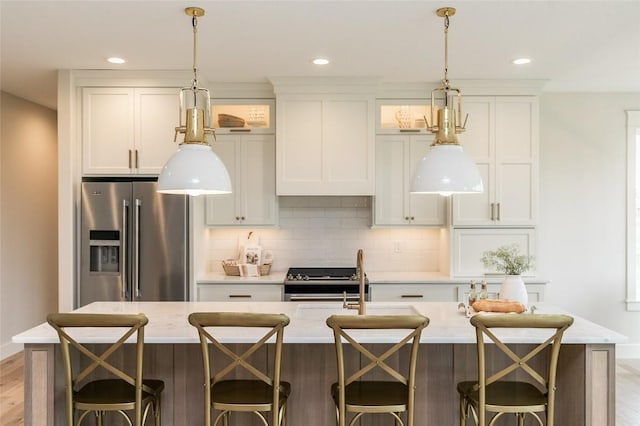 kitchen featuring an island with sink, decorative backsplash, light countertops, appliances with stainless steel finishes, and a kitchen breakfast bar