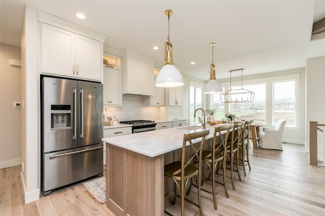 kitchen featuring an island with sink, a sink, stainless steel appliances, white cabinetry, and tasteful backsplash