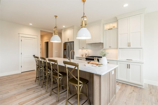 kitchen featuring high end appliances, a center island with sink, decorative backsplash, light countertops, and light wood-style floors