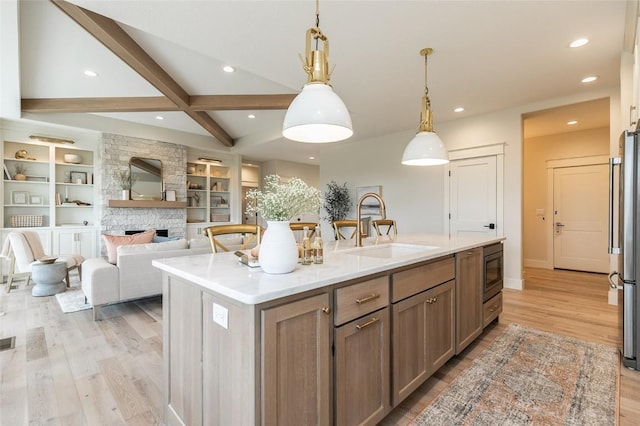 kitchen featuring black microwave, an island with sink, light countertops, light wood-type flooring, and a sink