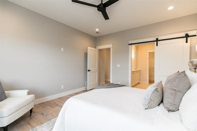 bedroom with baseboards, ensuite bath, light wood-style flooring, recessed lighting, and a barn door