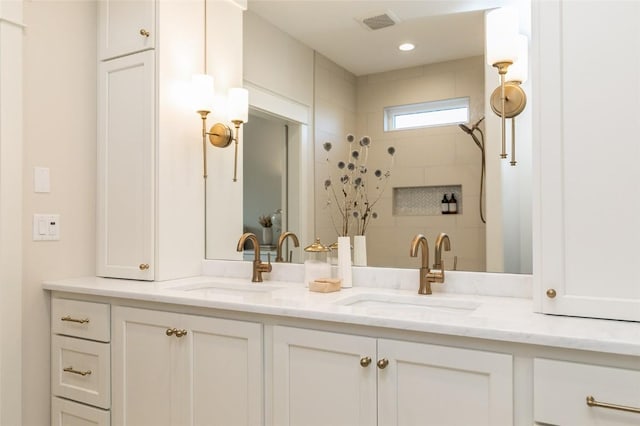 bathroom with double vanity, visible vents, tiled shower, and a sink