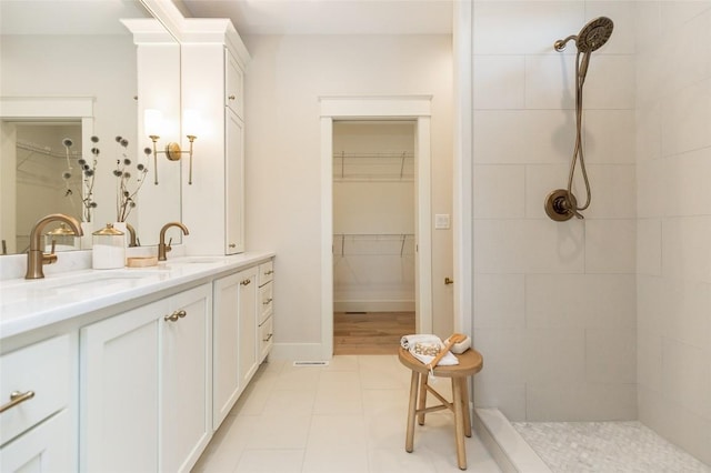 bathroom featuring a sink, tile patterned flooring, double vanity, tiled shower, and a spacious closet