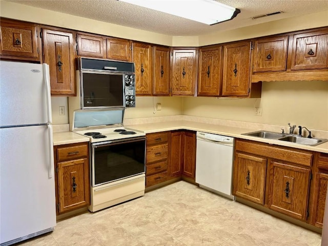 kitchen featuring a textured ceiling, white appliances, light countertops, and a sink