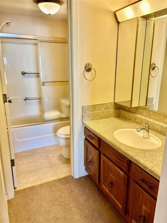 full bath with tile patterned flooring, enclosed tub / shower combo, toilet, and vanity