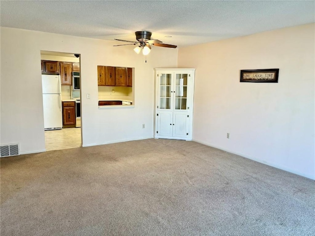 unfurnished living room with light carpet, visible vents, a textured ceiling, and ceiling fan