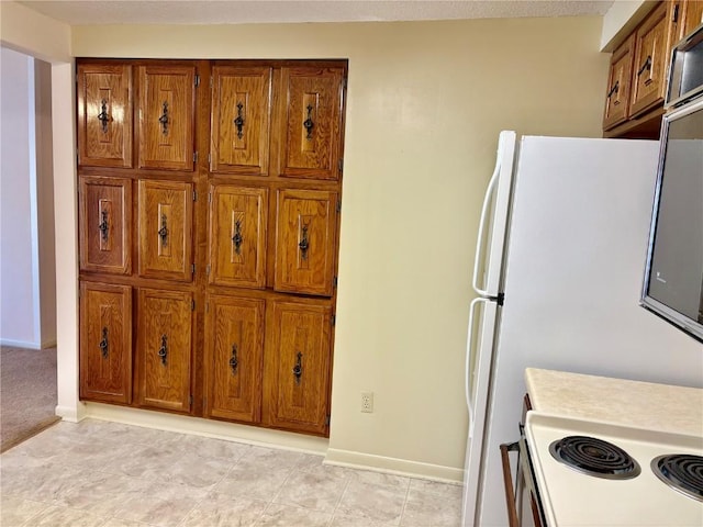 kitchen featuring brown cabinetry, freestanding refrigerator, light countertops, and baseboards