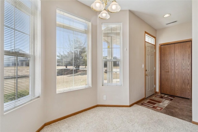 foyer featuring visible vents, baseboards, carpet, plenty of natural light, and a notable chandelier