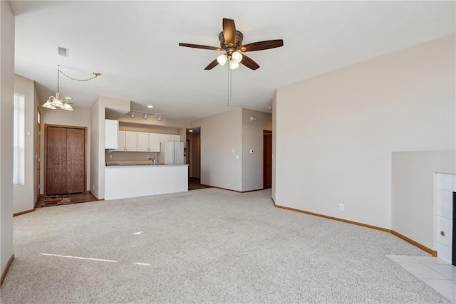 unfurnished living room with visible vents, baseboards, rail lighting, ceiling fan with notable chandelier, and light colored carpet