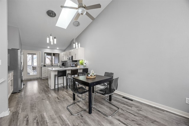 dining room with ceiling fan, visible vents, a skylight, and light wood-style flooring